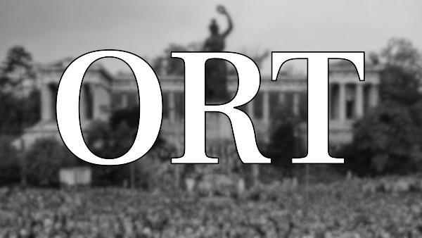 Der Schriftzug „ORT“ (für Orte) steht im Vordergrund. Der Hintergrund zeigt unscharf eine Versammlung vor der Bavariastatue in München.